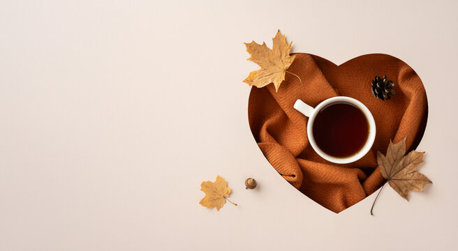 A heart-shaped arrangement with a cup of tea on a warm blanket, surrounded by autumn leaves, evoking a cozy and seasonal feeling