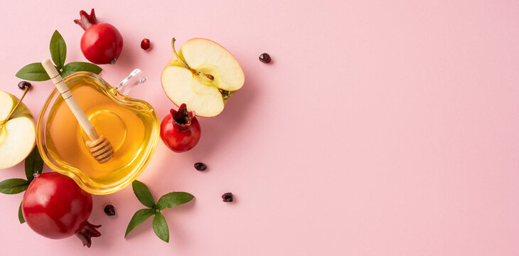 Jewish New Year celebration concept featuring traditional symbolic items like honey, apples, pomegranate, and greenery arranged over pink surface