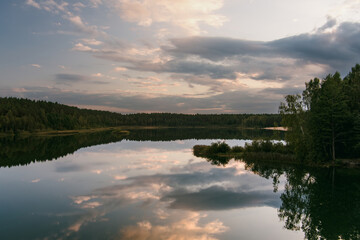 Lake Gela in Lithuania reflects dramatic clouds and surrounding forest in its calm waters, creating a serene and moody landscape