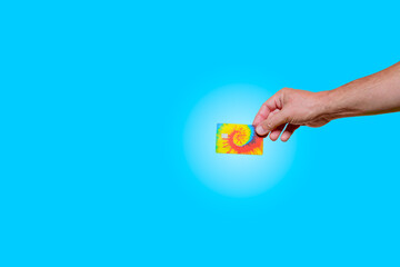 Male hand holding tie-dye credit debit card. Blue background. Copy space