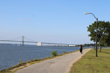 Relaxing Walk Along the Riverbank Near the Bridge on a Clear Sunny Day With Lush Greenery and a Peaceful Atmosphere
