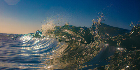Inside curling ocean wave with sunlight reflections
Close-up view inside a curling ocean wave with golden sunlight illuminating the translucent turquoise water, creating a vivid and dynamic seascape

