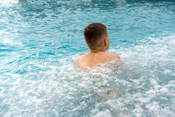 Happy boy enjoying refreshing swim in blue pool with splashing water on summer day. Concept of...