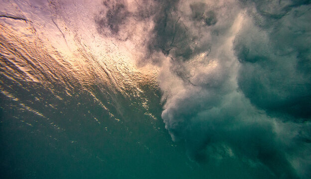 Underwater view of water surface below surfing wave breaking in bubbles and foam 