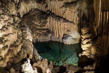 Majestic stalactites and stalagmites in illuminated underground cave pool