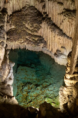 Mysterious underground cave with stalactites and crystal clear water pool