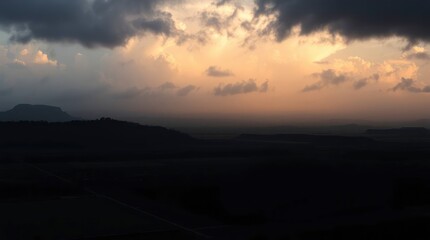 Obraz premium Dark landscape with a line of hills and lowlying clouds under a sunsetcolored sky