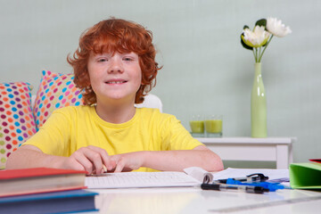Homework at Home. A young boy smiling happily while doing homework at a table at home. He is...