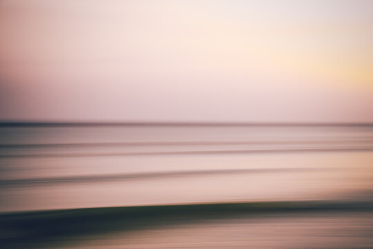A blurred view of the ocean at sunset in soft purples and pinks.