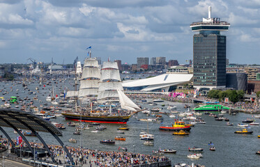 A vibrant view of Amsterdam Central Station with NS trains, trams, and a large crowd gathered along...