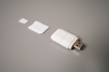 Fototapeta premium Close-up of white micro sd card reader featuring usb connector resting on gray table, accompanied by adapter and microSD card, highlighting compact and portable design