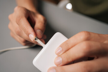 Technician hands inspecting damaged charging cable, revealing connectivity risks from visible cable fraying and potential electrical safety concerns, sitting at desk in workshop.
