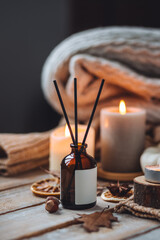 Home comfort, coziness, aromatherapy. Cozy interior with knitting, burning candles and aroma perfume diffuser in the living room. Fall scent, sweet pumpkin pie fragrance, dry leaves, autumn mood