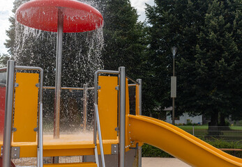 Colorful water playground equipment with red mushroom fountain and orange slides creating...