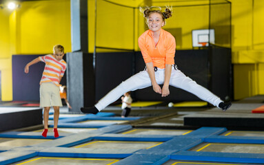 Cheerful teen girl in sport clothes bouncing on trampolines indoors in leisure sport center for kids