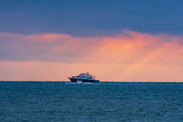 The sun's rays hit a boat sailing in the middle of the sea.