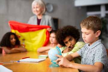 Fototapeta premium Portrait of a schoolboy in class, studying the history of the country of Spain in lesson and looking for it on the globe