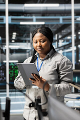 Woman in data center doing software updates, verifying deep learning parameters. African american...