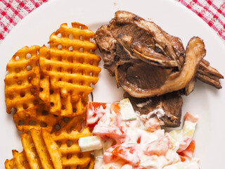 Dinner meal with cooked lamb loin chops, potato lattice and fresh salad with sour cream. Close up....