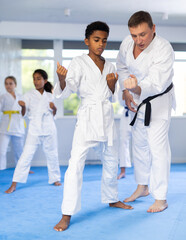 Experienced coach demonstrating technique of punches to focused african american boy during kata at...