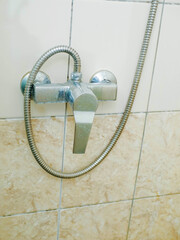 A shower head with a silver hose attached to it. The shower head is old and rusty. The bathroom is...