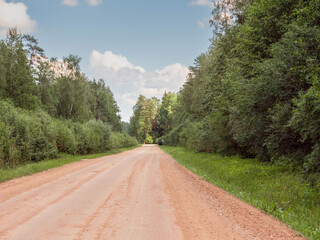 A dirt road with tree forest on each side and in the background. The road is empty and there is no...