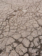 A cracked and broken road with a lot of holes and cracks. The road appears to be in a state of disrepair and is not safe for driving. The cracks and holes are scattered throughout the road