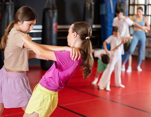 Teenage girls practice self-defense techniques during sparring. Children learn holds during...