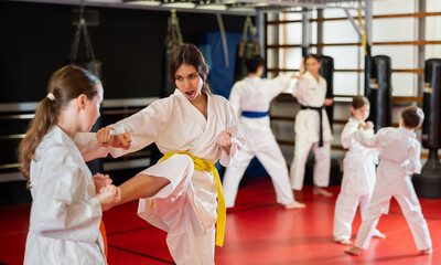 Teenage girls are actively engaged in judo. Children in white kimonos at a martial arts training session