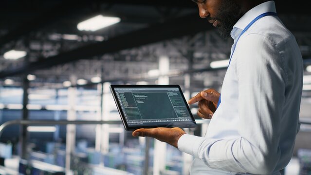 Close up of programmer swiping on tablet display in data center, doing maintenance tasks, ensuring optimal performance. IT expert checks code on device, applying patches to improve stability