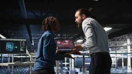 Stressed technicians in server room fighting each other after detecting hacking attempt targeting critical systems. Engineering team members under pressure by virus activity arguing,