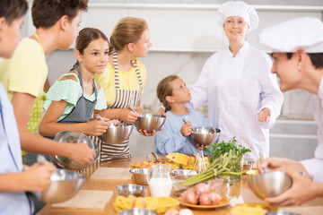 During cooking classes, teen girl stands on other side of table from cook guy and looks at him...