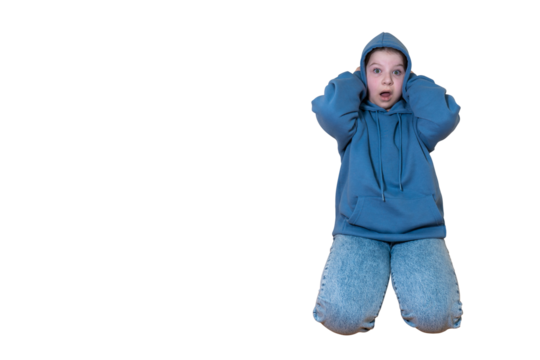 Shocked young girl in blue hoodie and jeans covering ears with hands and with open mouth on transparent background