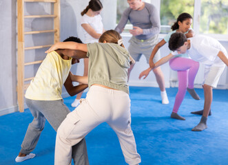 Girls and boys practicing in pair self-defence movements with male trainer supervision