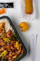Flat lay of Asian takeout food featuring chicken stir fry with broccoli and peppers, white rice, fried egg roll, fortune cookie, and dipping sauces. Fast food concept on clean minimal background.