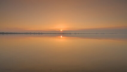 Naklejka premium Misty Sunrise Over Calm Water Reflection