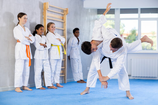 Adult man coach and boy in kimono practicing judo techniques in studio.. - Powered by Adobe
