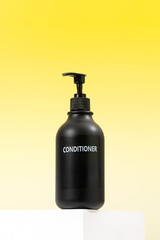 A black mock-up of a hair conditioner on a podium on a yellow background. Hair care.