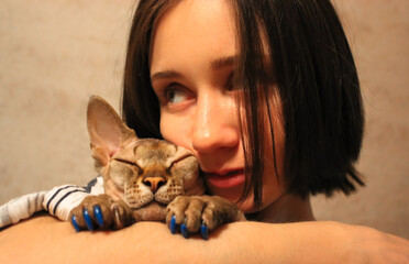 A young woman shares a tender moment, cuddling with hairless Sphynx cat. A brunette girl tenderly embraces a lovable cat in a moment of affection. The cat has blue nails National Cat Day, October 29th