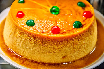 Coconut flan dessert topped with colorful cherries, displayed in a festive cafe-pastry shop, creating a warm and inviting holiday atmosphere for seasonal celebrations
