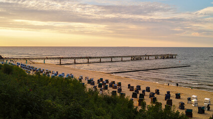 Obraz premium Koserow pier on Usedom with beach chairs on the sandy shore shortly before sunset – tranquil Baltic Sea seaside scene.