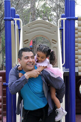 Single dad and 4-year-old Latina daughter with curly brunette hair play on playground and spend...