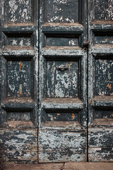 Close-up of peeling blue paint on weathered wooden shutters showing aging texture