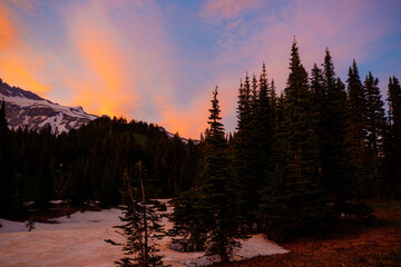 Stunning sunset over Mount Rainier, Washington. Vibrant sky with warm hues illuminating the rugged mountain peaks and surrounding forest.