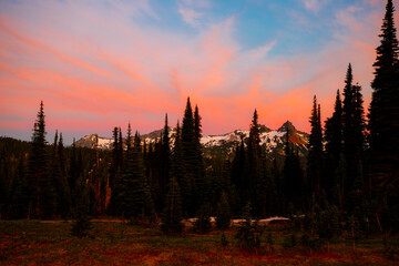 Stunning sunset over Mount Rainier, Washington. Vibrant sky with warm hues illuminating the rugged mountain peaks and surrounding forest.