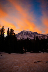 Stunning sunset over Mount Rainier, Washington. Vibrant sky with warm hues illuminating the rugged mountain peaks and surrounding forest.
