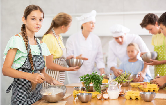 Girl in apron learning to cook at cooking master class - Powered by Adobe