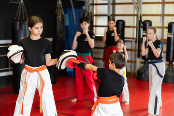 Boy in boxing gloves trains boxing punches with teenage girl in boxing mitts in studio