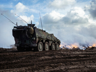 Military wheeled armored vehicle positioned during training with smoke screen effects in background