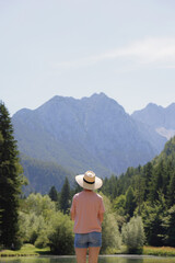 A person stands by a tranquil lake, gazing at majestic mountains under a clear blue sky surrounded...